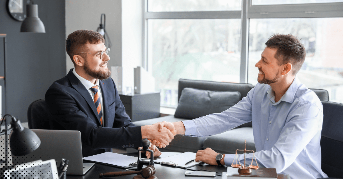 Two business professionals shaking hands and smiling during a meeting in a modern office setting.