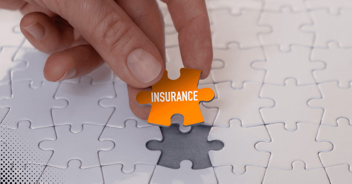A hand placing an orange 'insurance' puzzle piece into a jigsaw puzzle, symbolizing the fitting of insurance coverage.