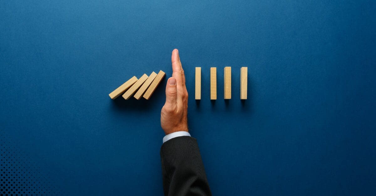 Hand stopping falling wooden blocks with a blue background.